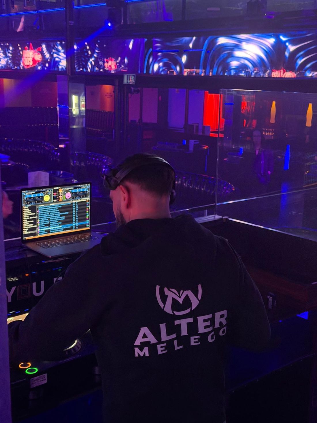 Alter Melego mixing in a club lit in blue and red